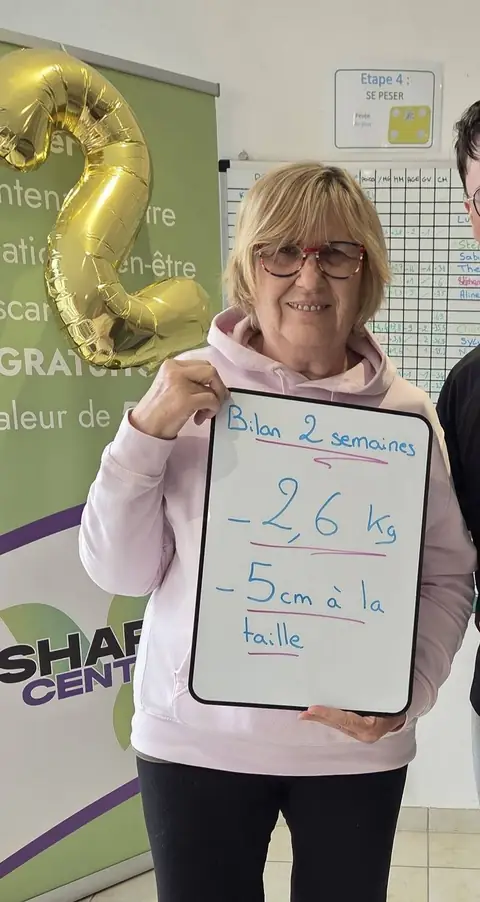 Une membre sourit devant son bilan noté sur l’ardoise, au club
